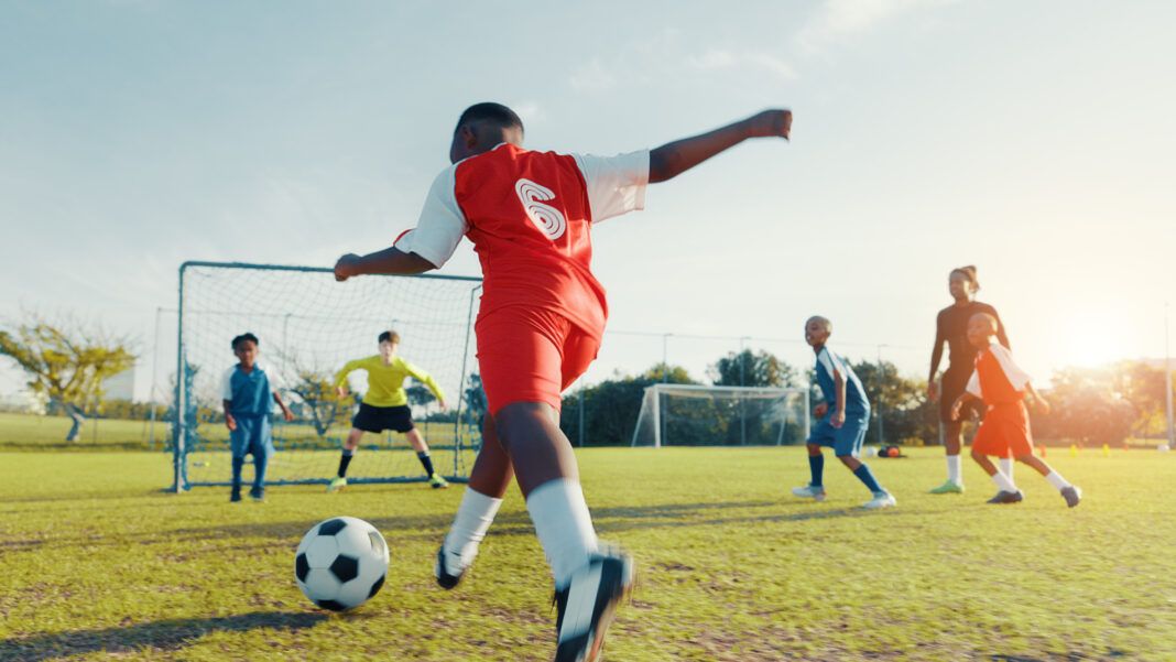 Sports field, goal and soccer player with skills, children and athlete with energy for match and cardio. Playing, football and kids with sportswear for game, growth and development of boys or fitness